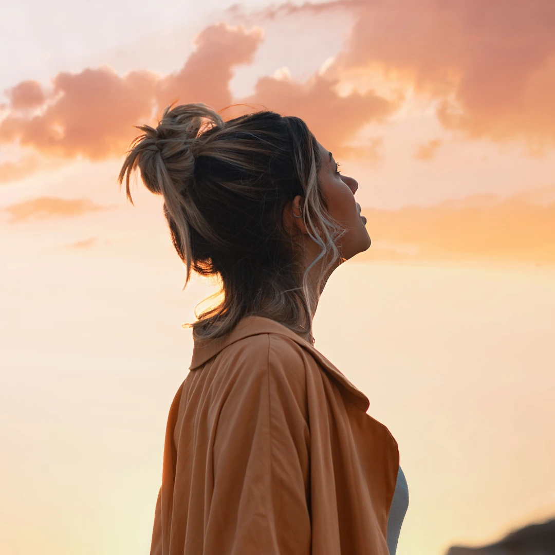 Eine junge Frau blickt optimistisch in den Himmel, strahlt Hoffnung und Zuversicht aus.